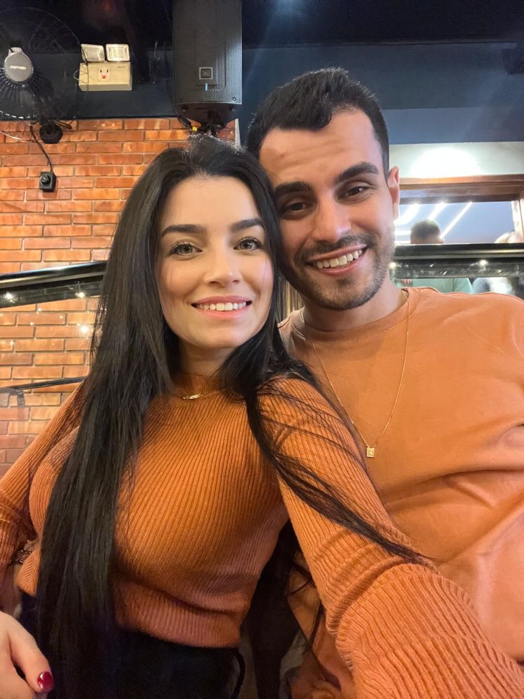 O casal de suéter laranja, em frente a uma parede de tijolos