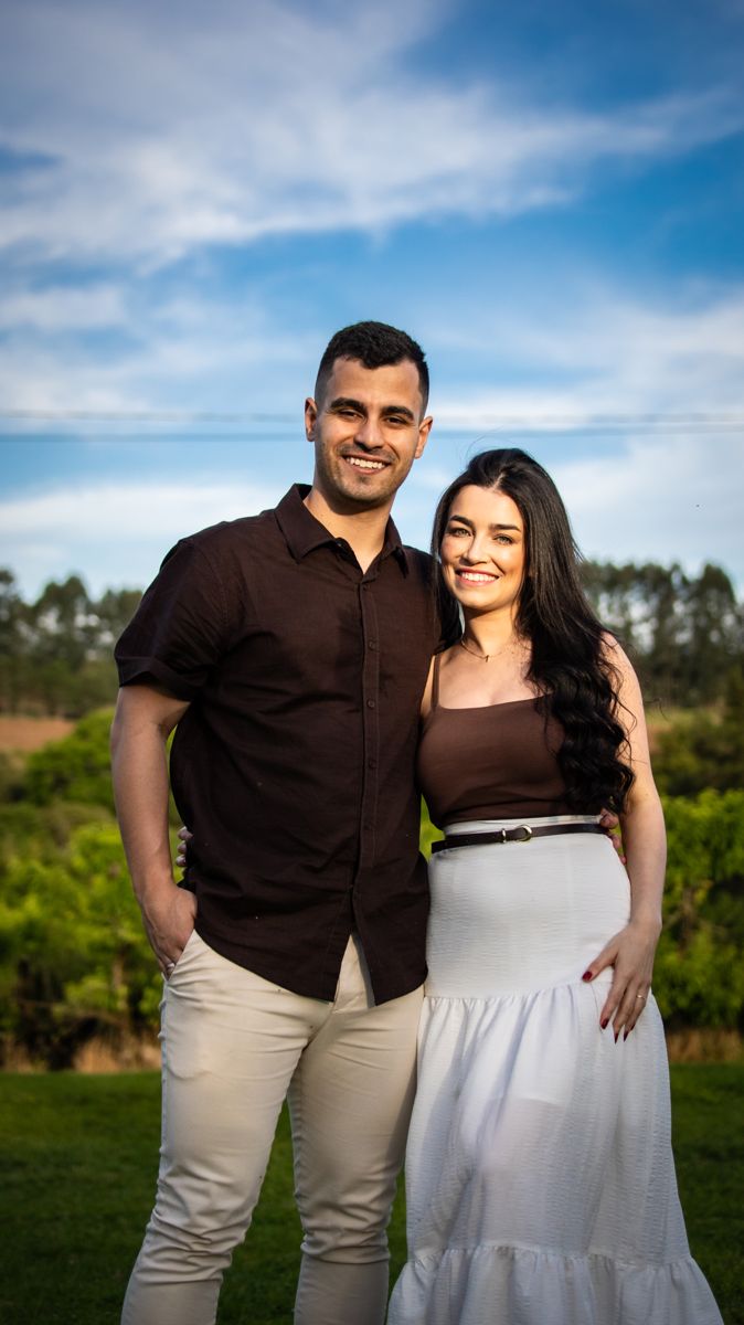 Juliana e Matheus abraçados, sorrindo, sob o céu azul