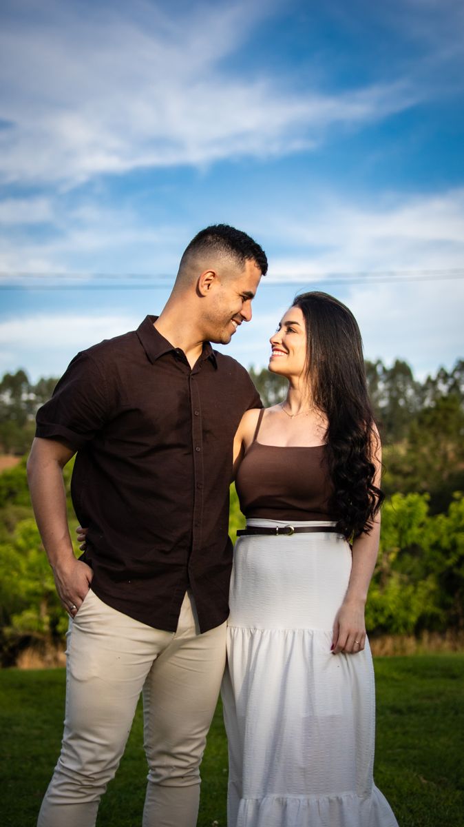 Juliana e Matheus abraçados, sorrindo, sob o céu azul